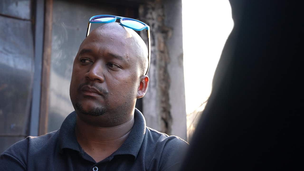 A man wearing a blue polo shirt looks to his right. He has a neutral facial expression and a pair of blue sunglasses on top of his head.