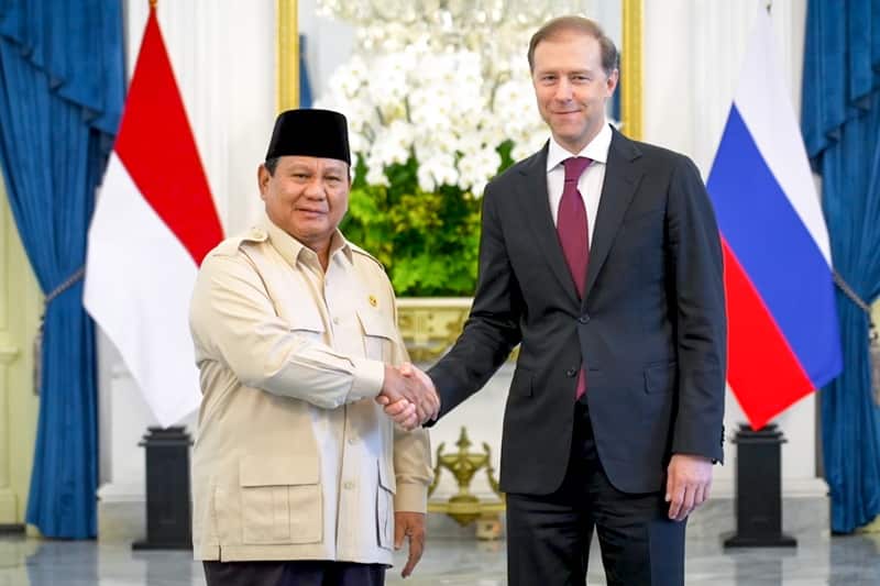 Two men pose for a photo while shaking hands. 