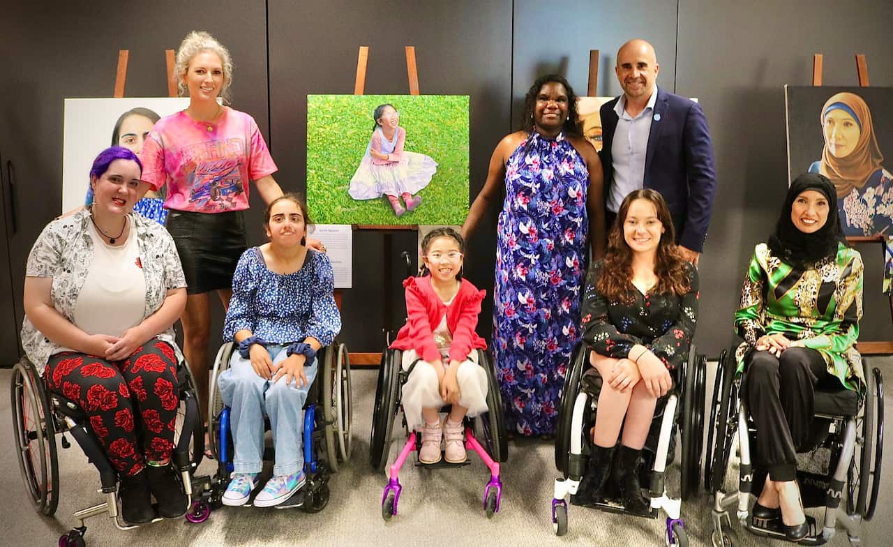 A group of people, some using wheelchairs, gathered around a series of paintings