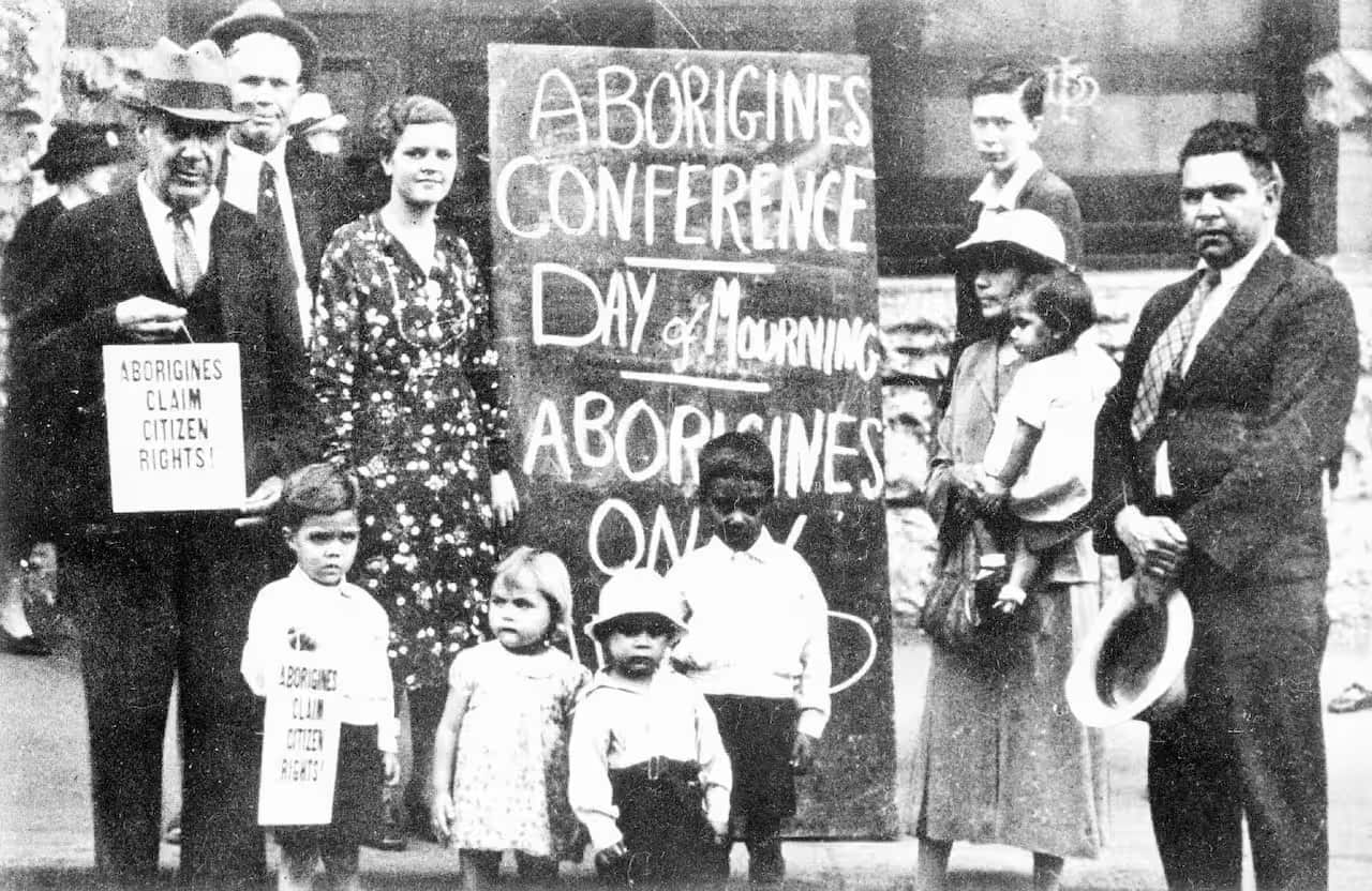 First Nations adults and children stand in a group in front of a sign during a January 26 in 1938.