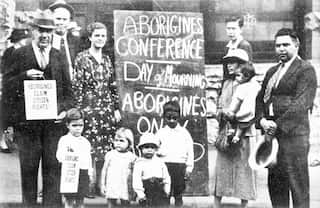 First Nations adults and children stand in a group in front of a sign during a January 26 in 1938.