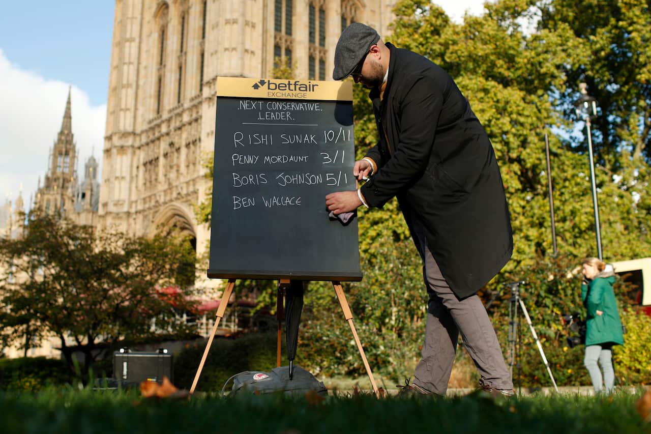 A man writing on a blackboard outside 