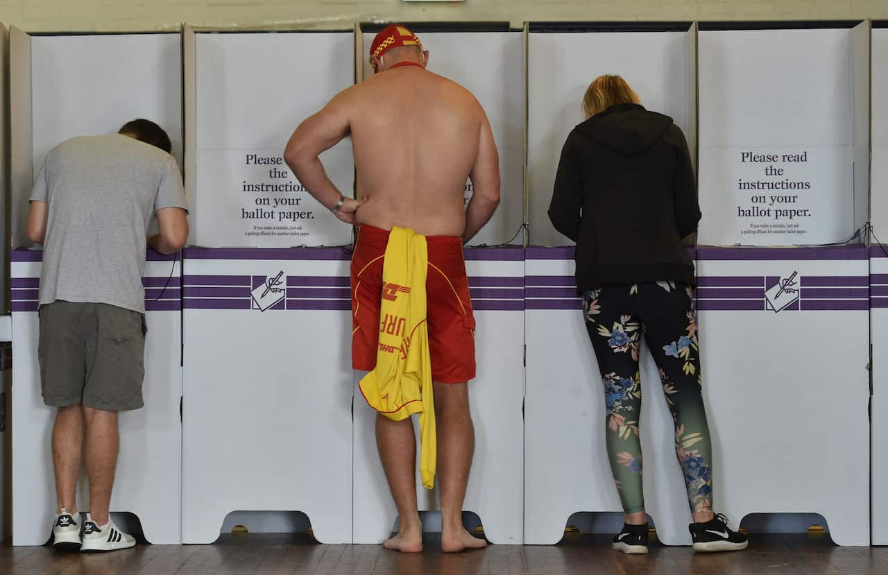 Two men and a woman with their backs towards the camera are voting on a ballot paper. 