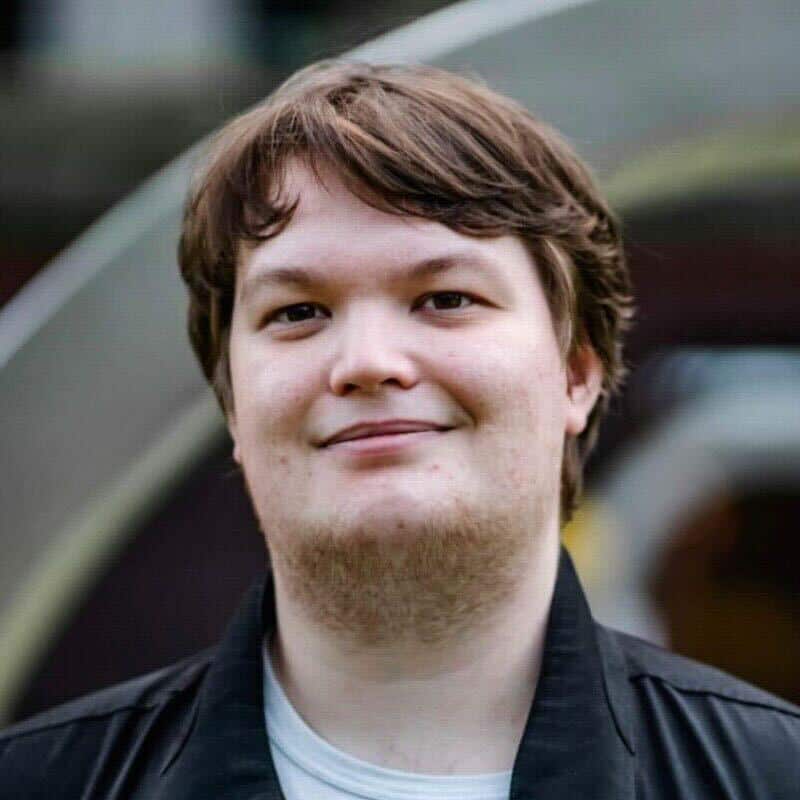 A man wearing a black shirt over a white t-shirt is smiling.