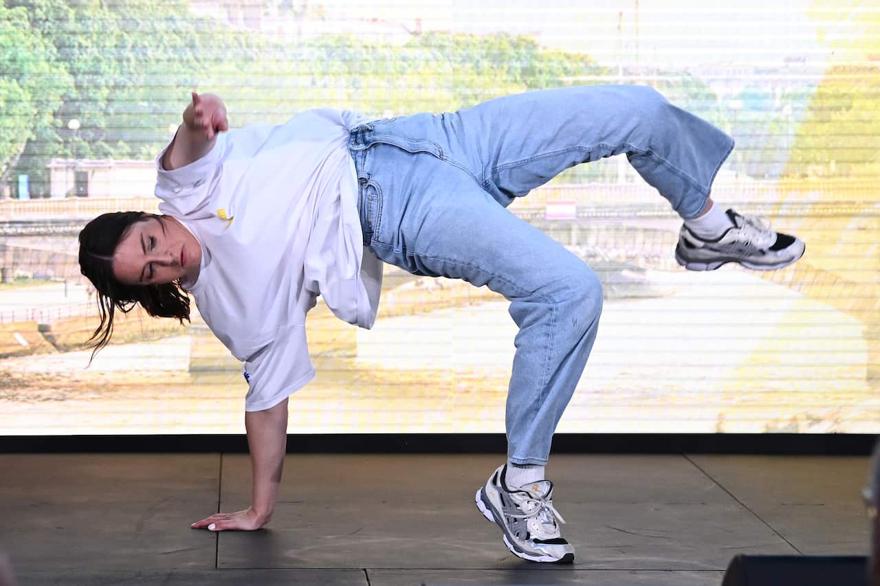 A woman in a white shirt and jeans dancing, with one hand and foot on the ground