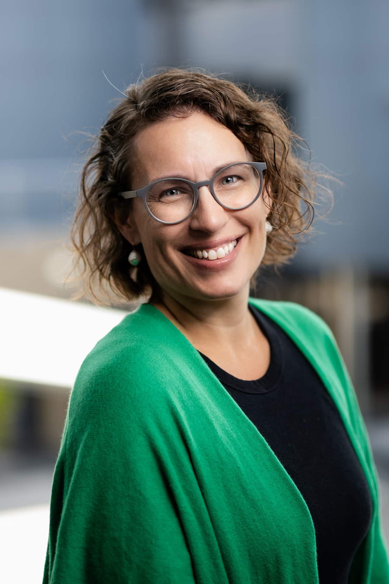 A woman in a green shrug worn over a black top is smiling.