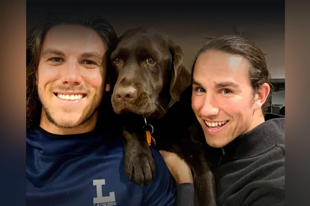 Two men with brown hair posing for a photo with a brown dog.