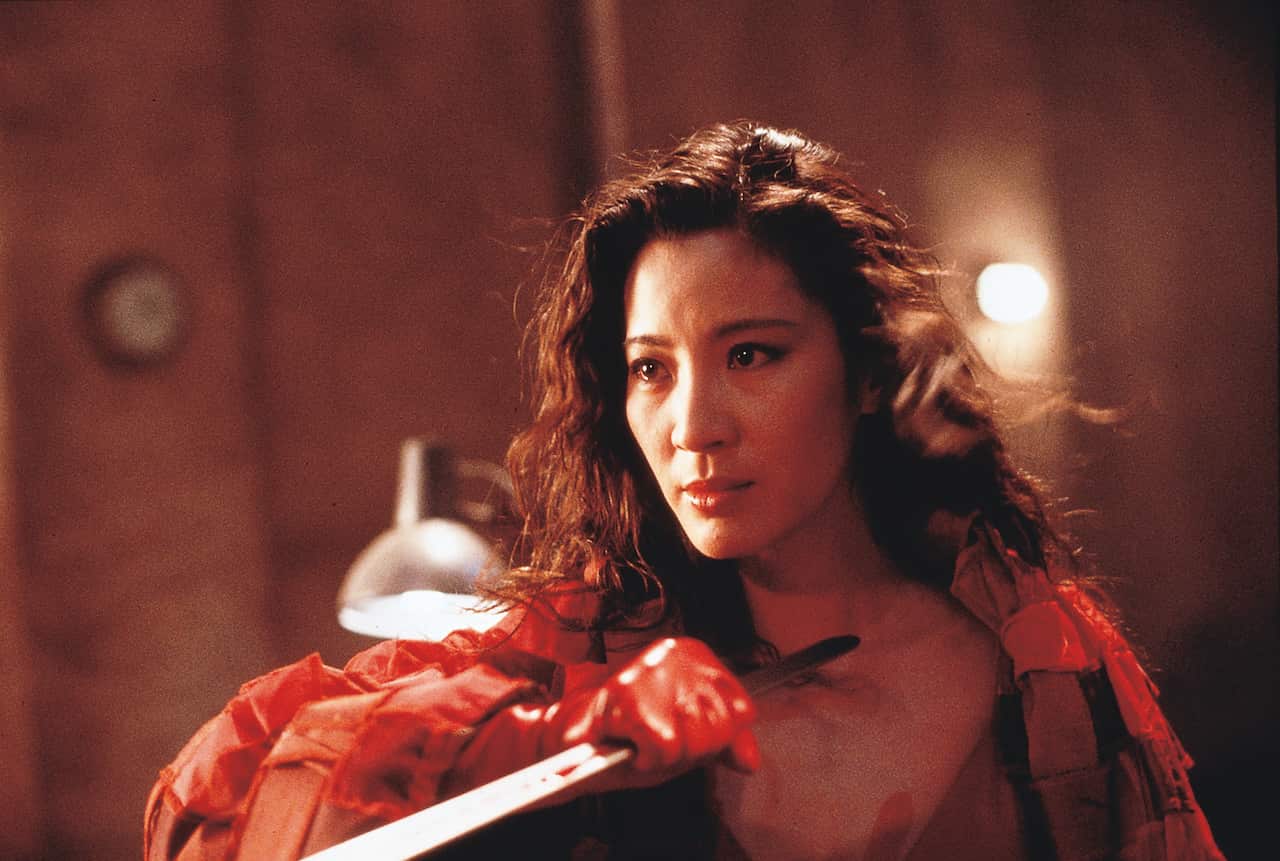 A woman with flowing dark hair in a red robe holds a bladke in front of her.