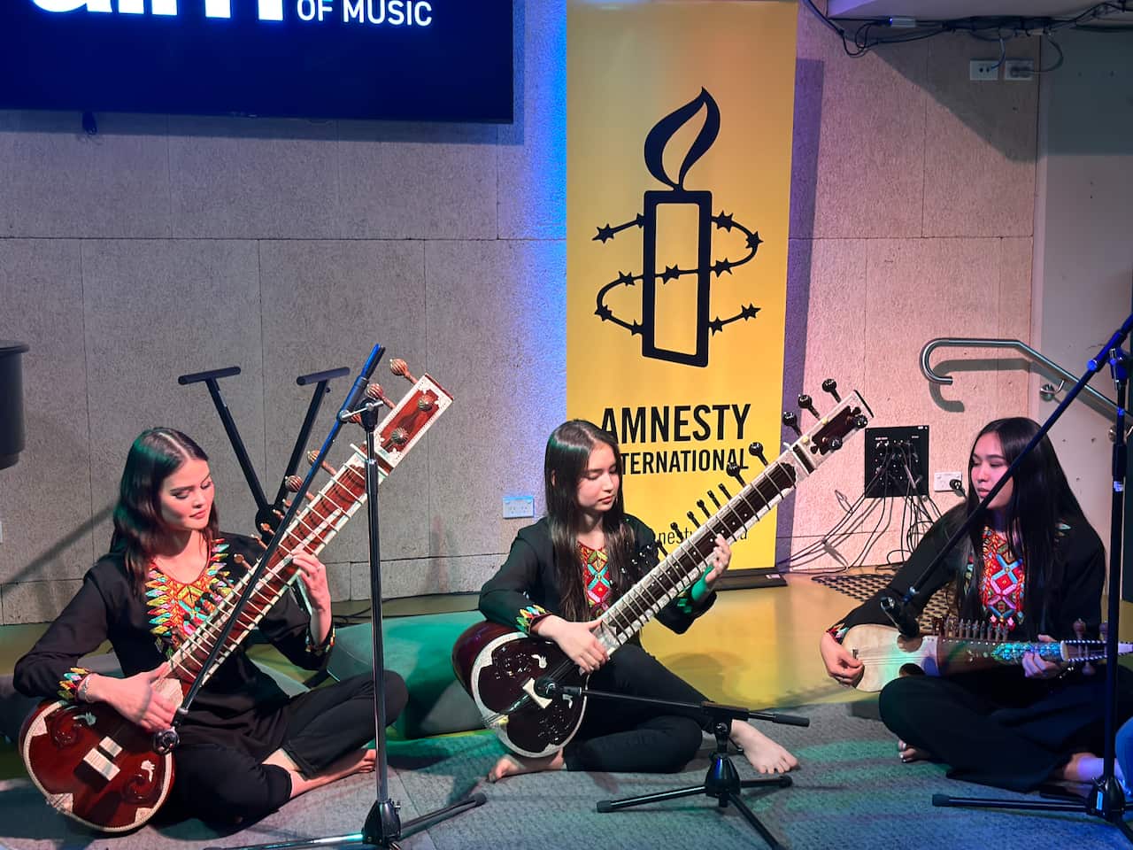 Three women sitting on the ground playing music.