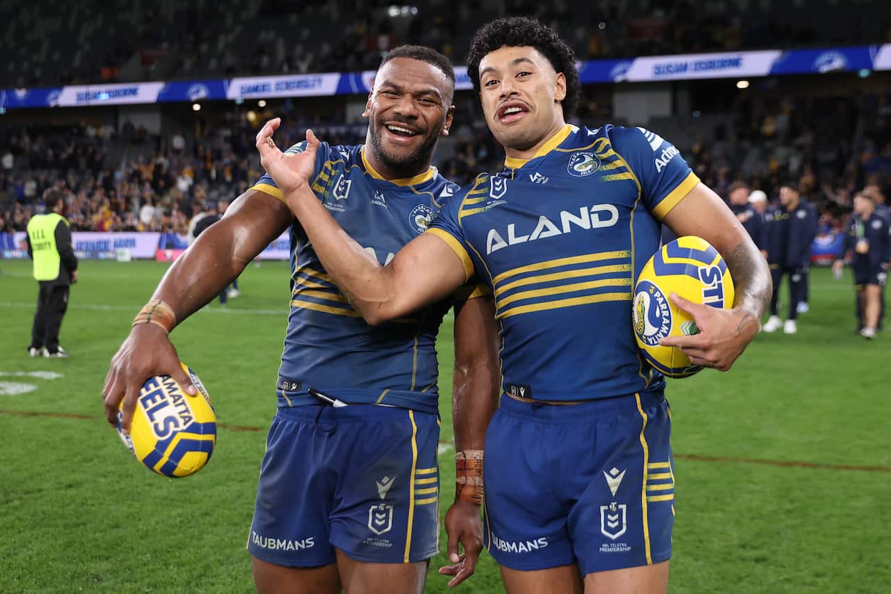 Two Parramatta Eels players smile while holding footballs 