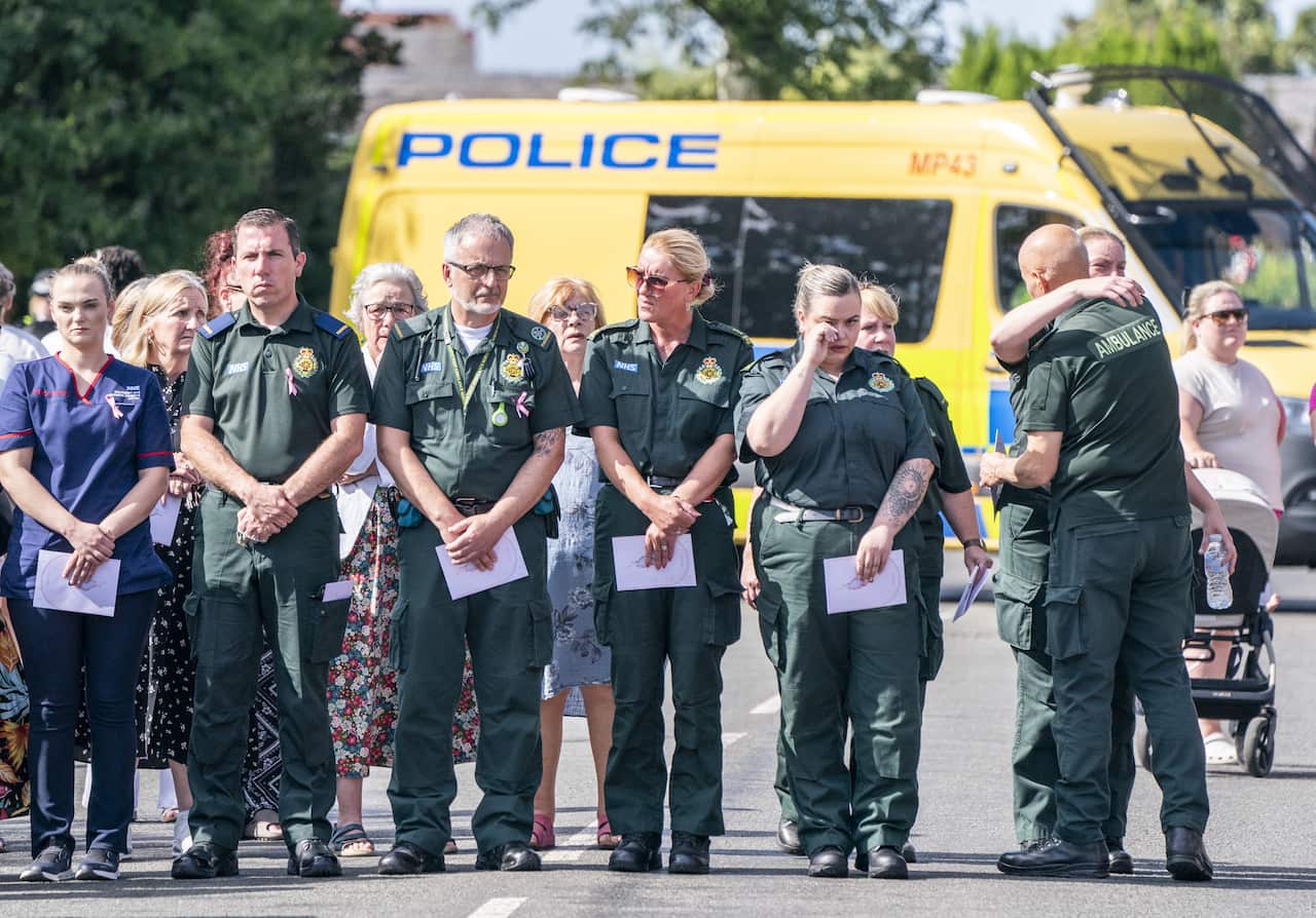 A line of people in green jumpsuits stand on a road