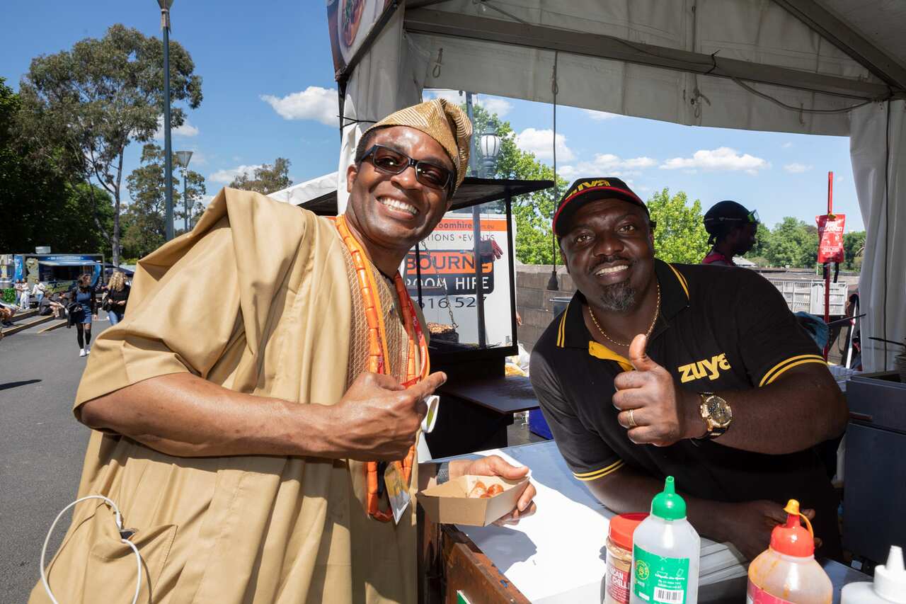 Two men pose for a photo as one man serves the other a meal from behind a food truck.