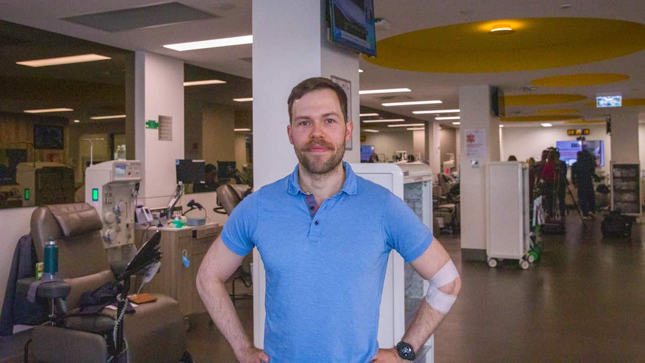 A man in a blue t-shirt and a white bandage around his elbow stands in the centre of a blood donation bank.
