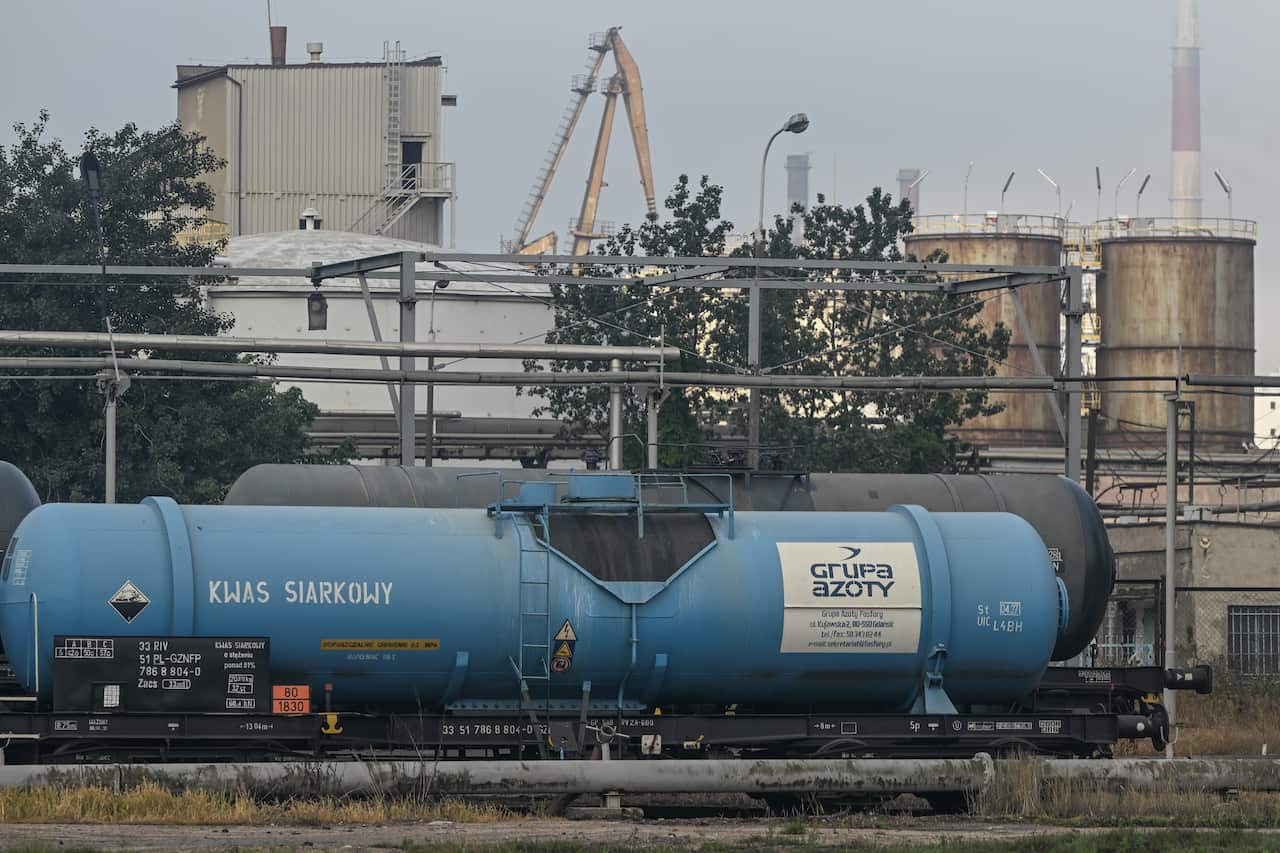 A blue railway tank car labeled "KWAS SIARKOWY" (sulfuric acid) and "Grupa Azoty" sits on a track in front of an industrial facility with storage tanks and cranes.