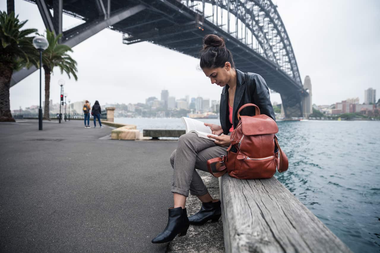 Woman reading a book sitting on a bench in Sydney Harbor