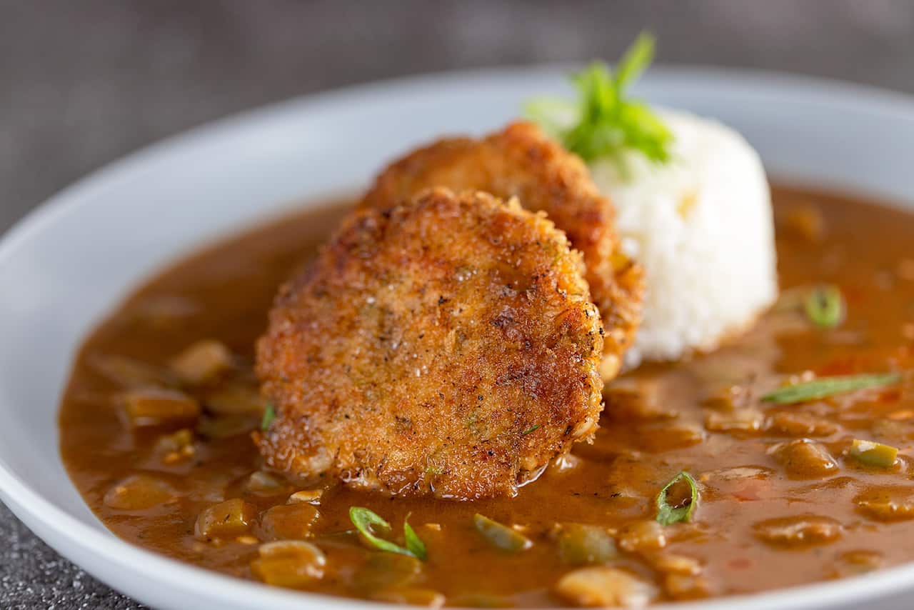 Two round crumbed patties sit in a bowl of red-brown soupy stew. 