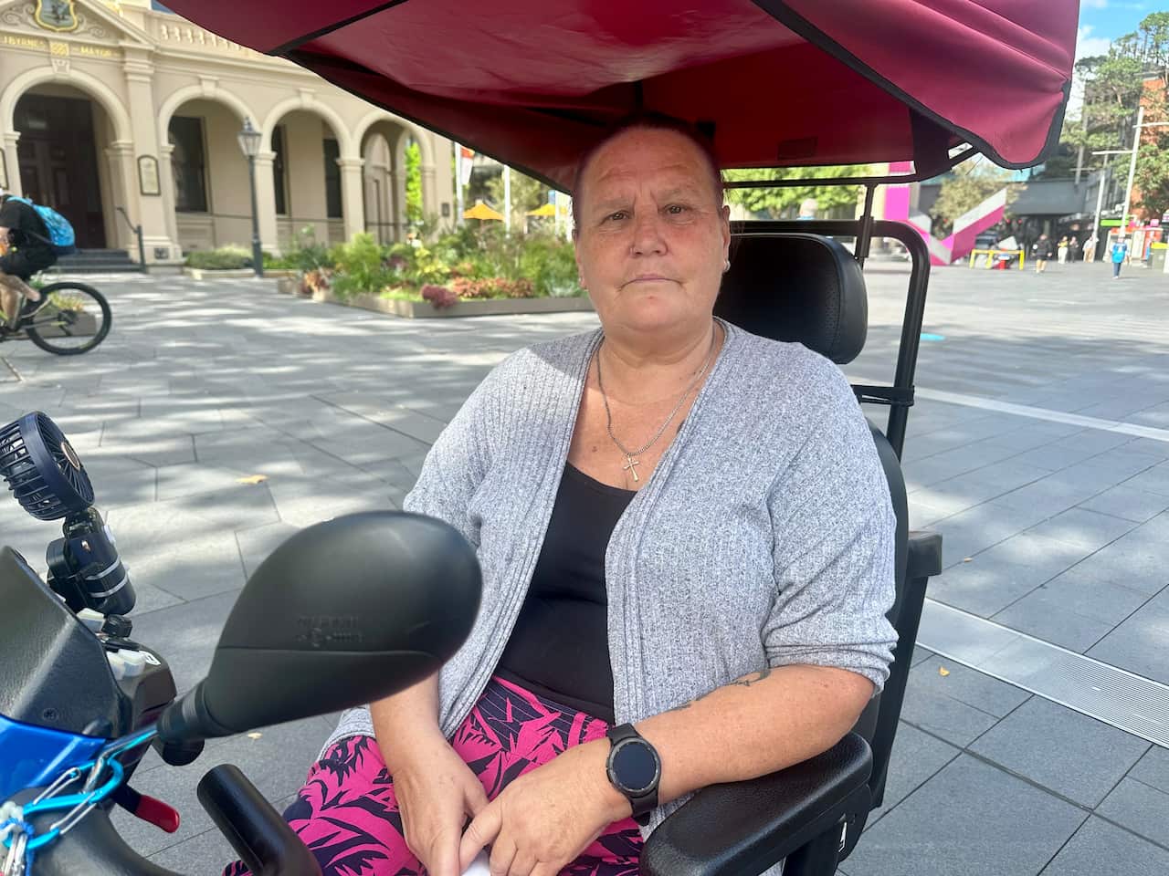 A woman in a grey sweater in a mobility scooter in a public square.