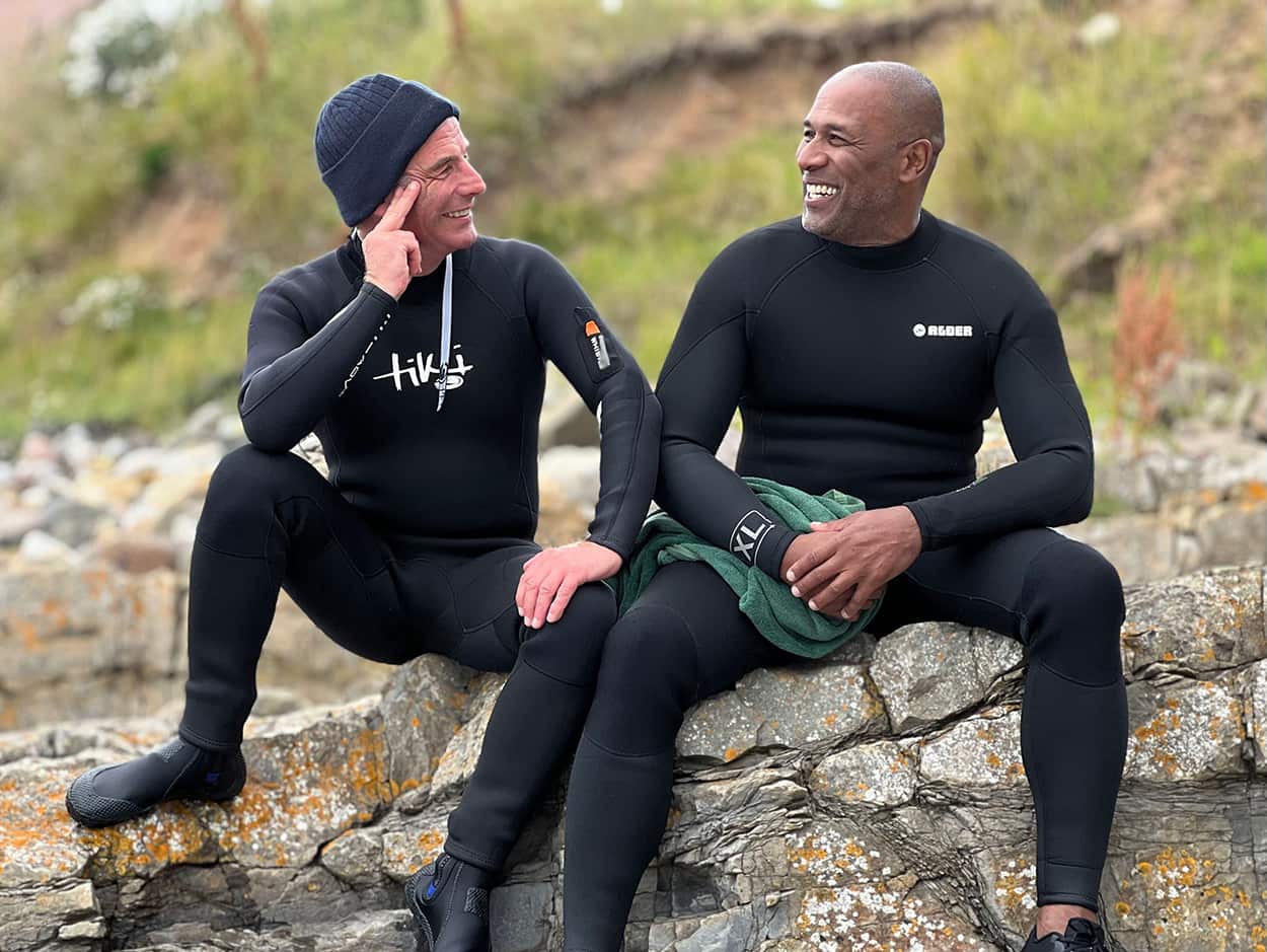 Two men sit on a rock in wetsuits in the north-east of England.jpg