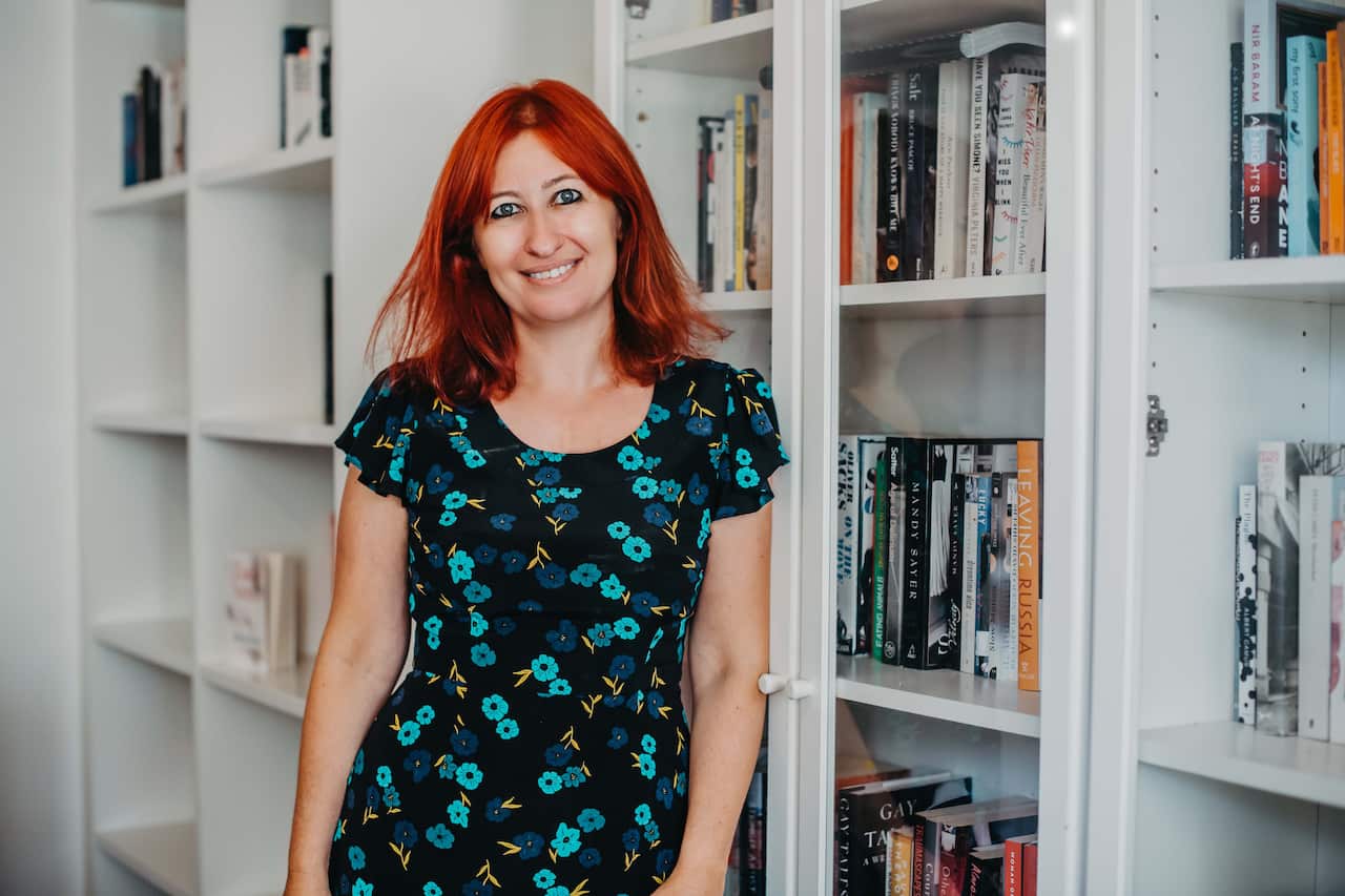 A woman leans against bookshelves.