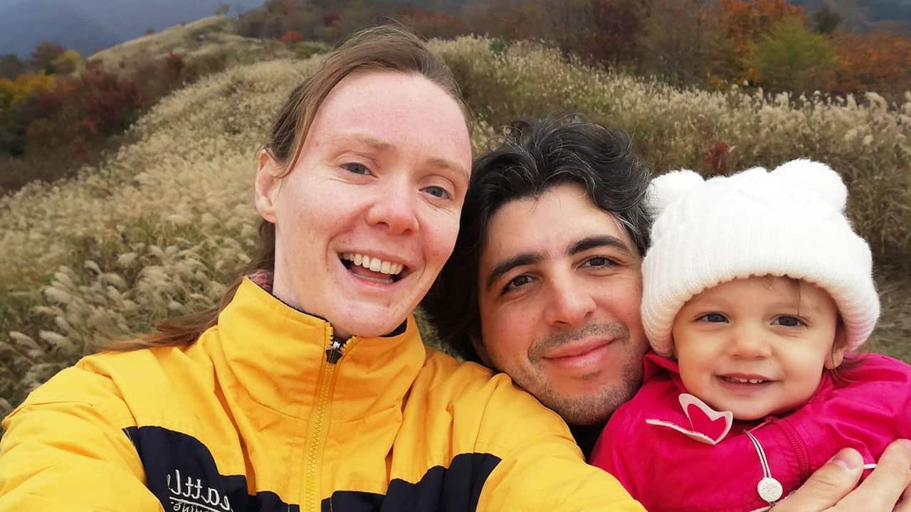 A woman in a yellow rain jacket taking a selfie with a man and a toddler wearing a pink jacket and a white beanie