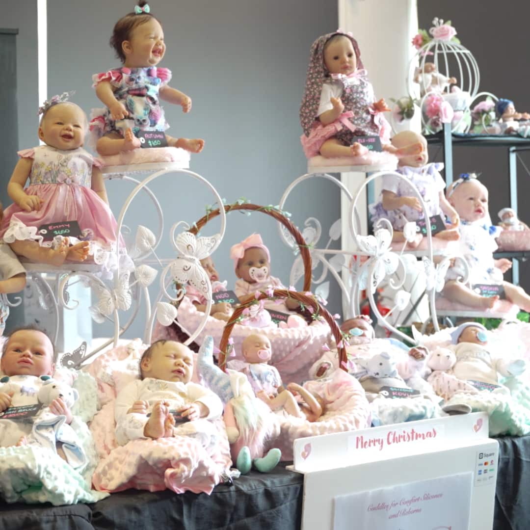 A table covered in a dozen reborn dolls displayed on pillows and in baskets