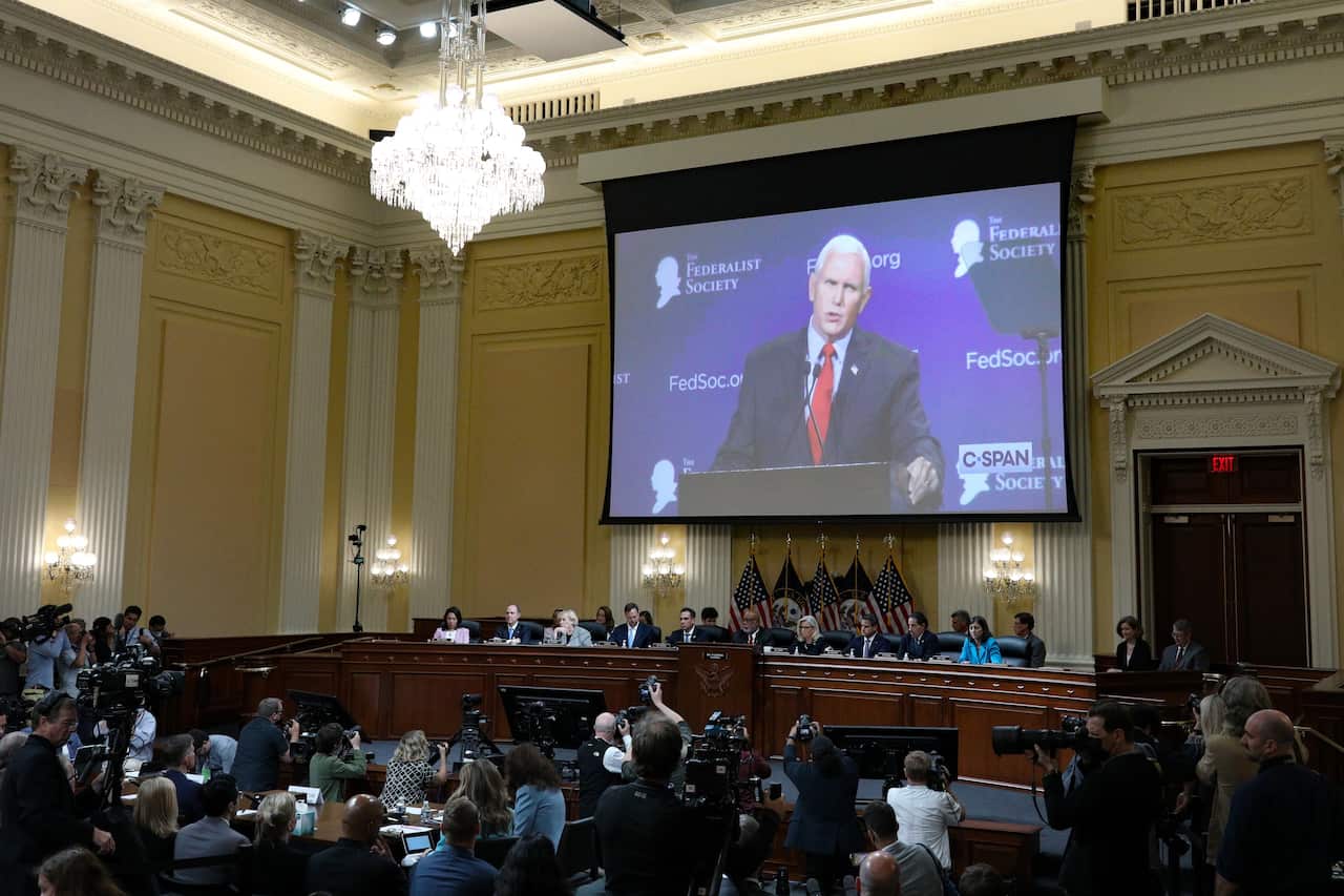 A man's face is projected on a large screen as several people look on.