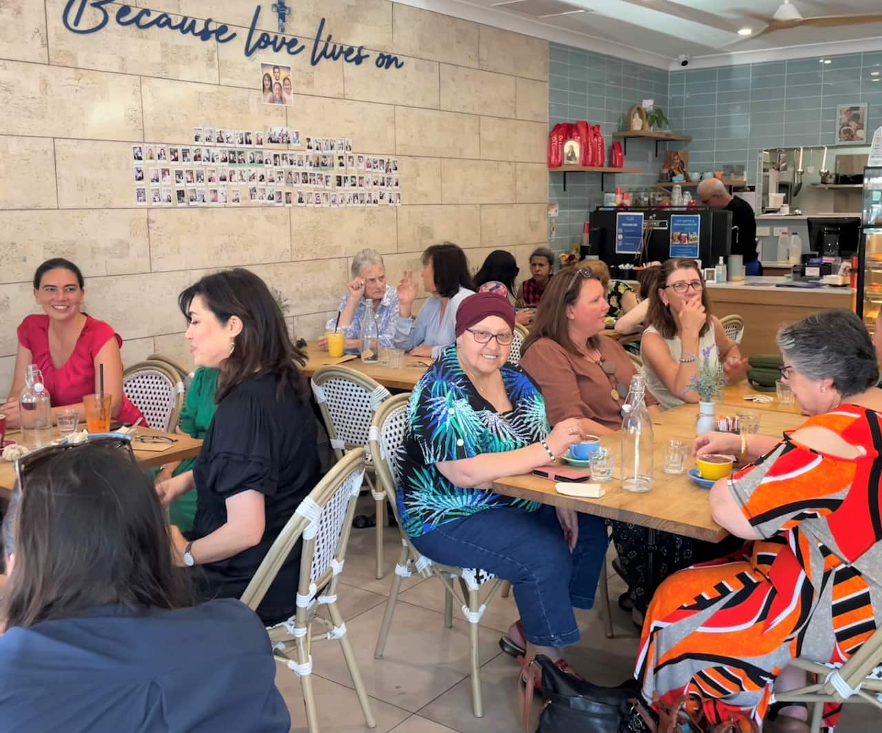 Customers sit at tables inside a cafe. There are photos on a wall. 