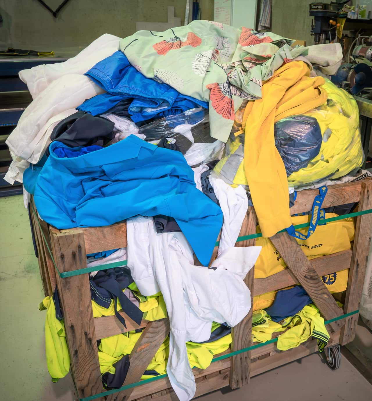A mound of colourful clothing in a wooden crate.