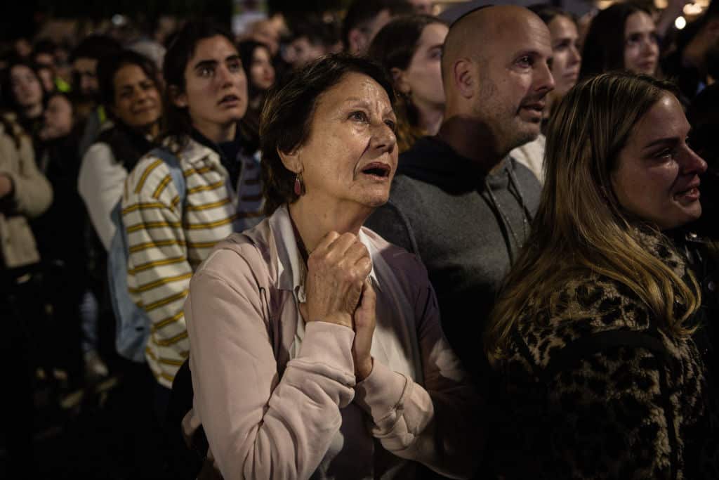 People watch a giant screen in a town square. 