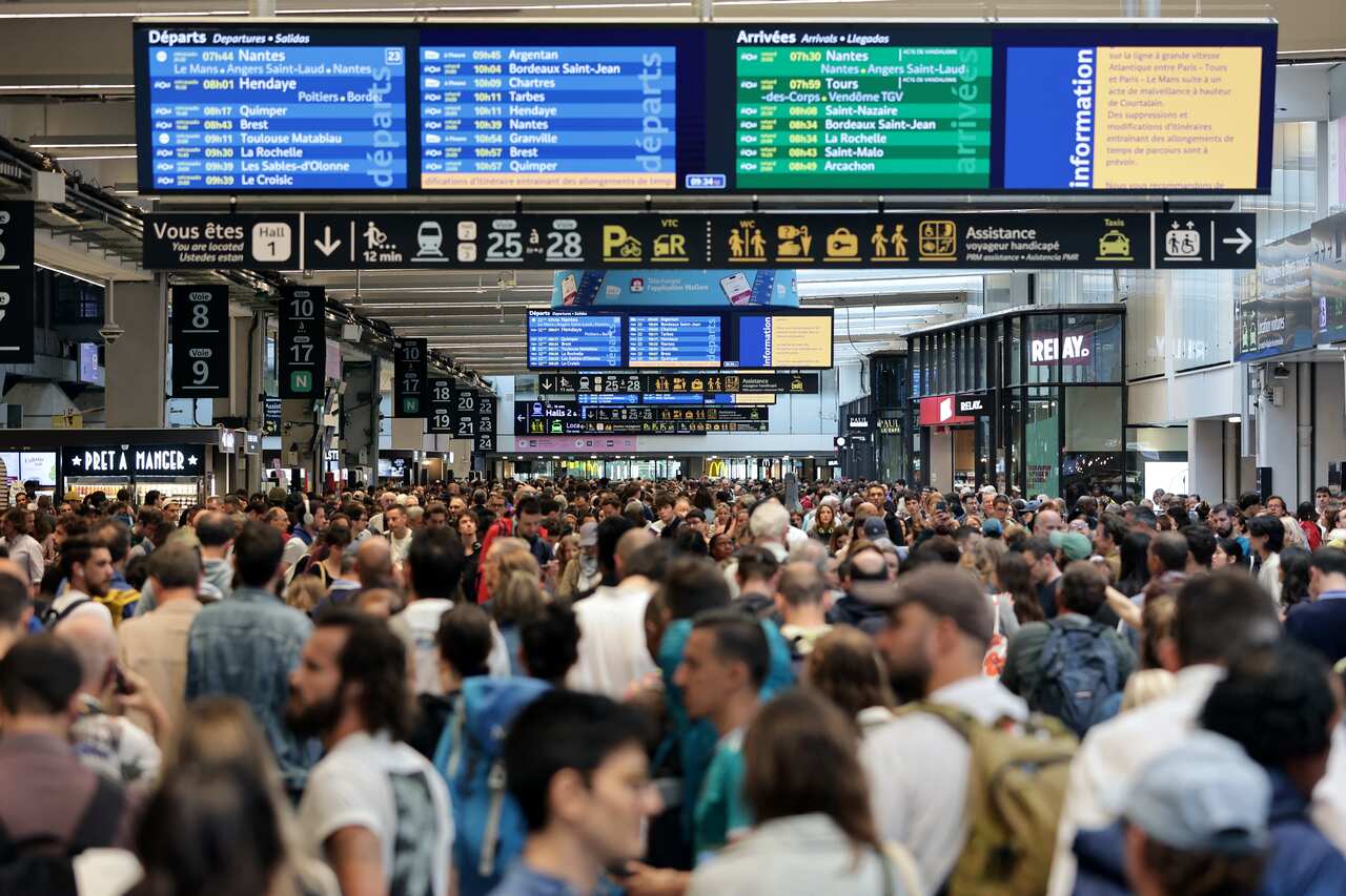 Passengers gather around the departure and arrival boards at a train station.