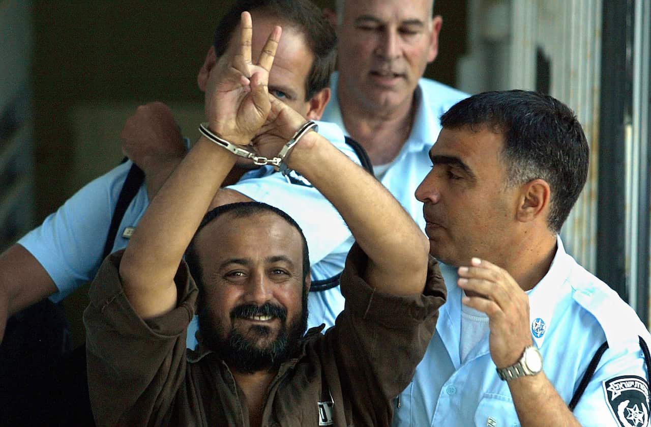 A man in handcuffs surrounded by uniformed guards