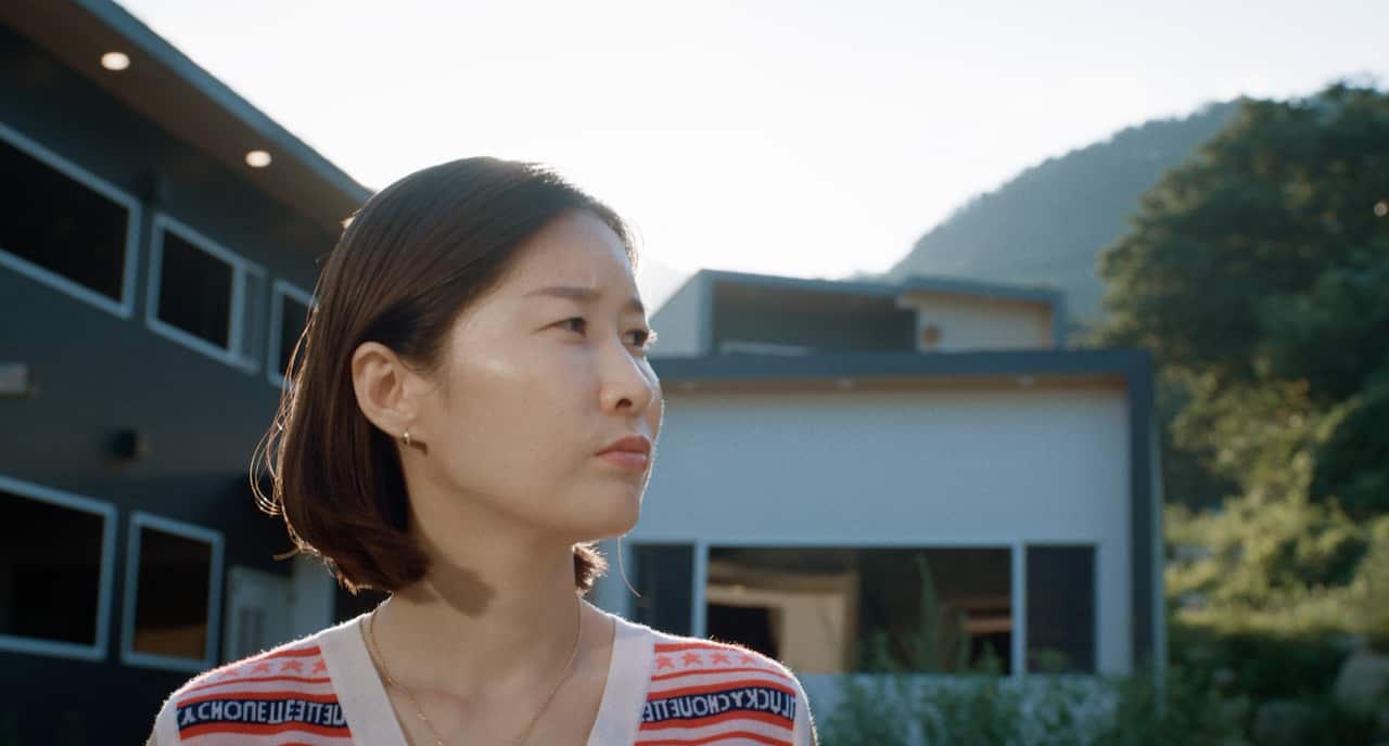 A woman looks to her right. She has short dark brown hair and is standing in front of a modern building. 