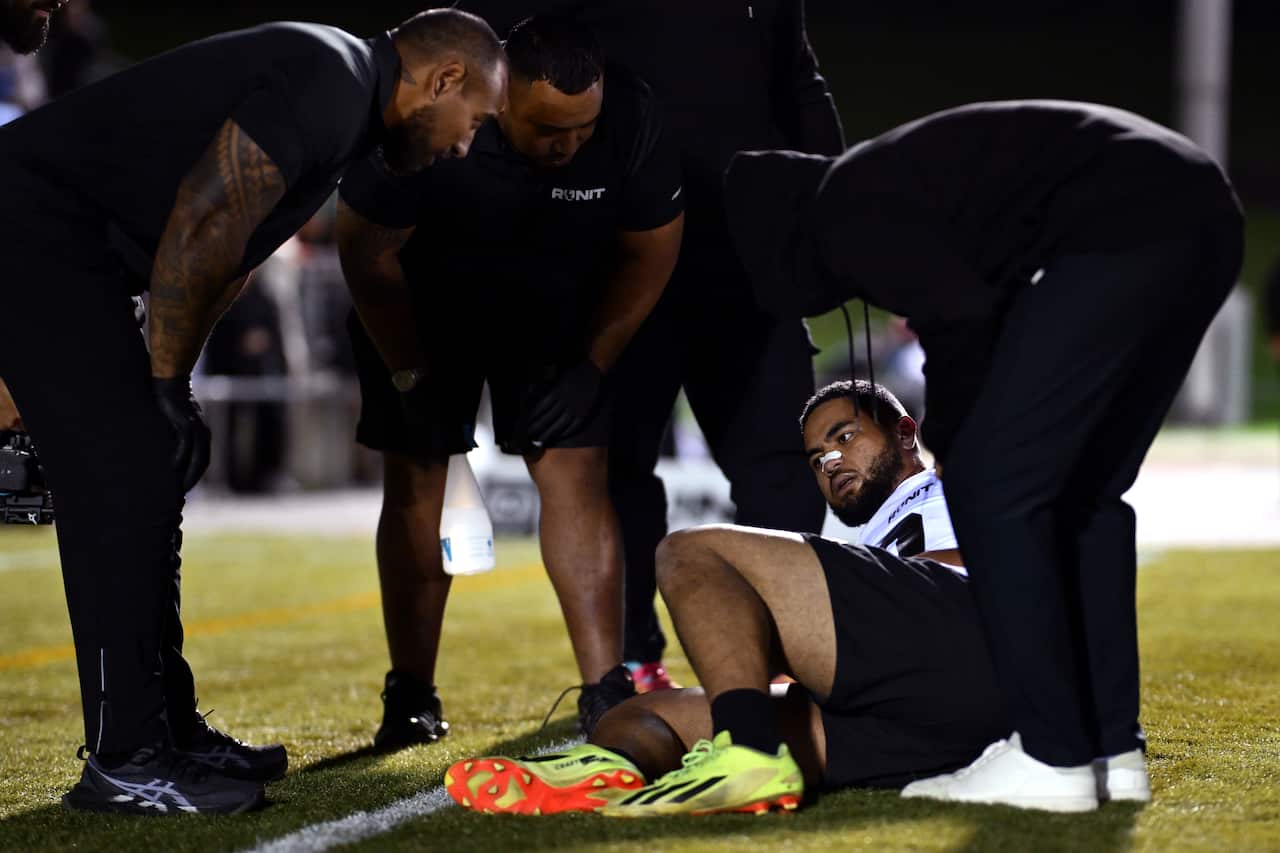 A man on the grounds of a grass playing field surrounded by four other men wearing black.