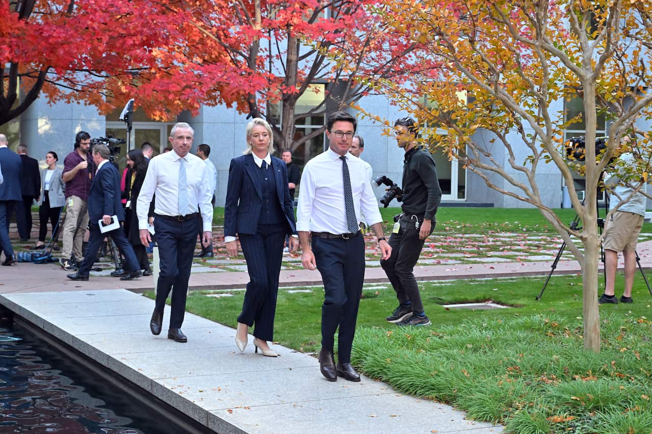 Two men wearing ties and woman wearing a blue suit walk.