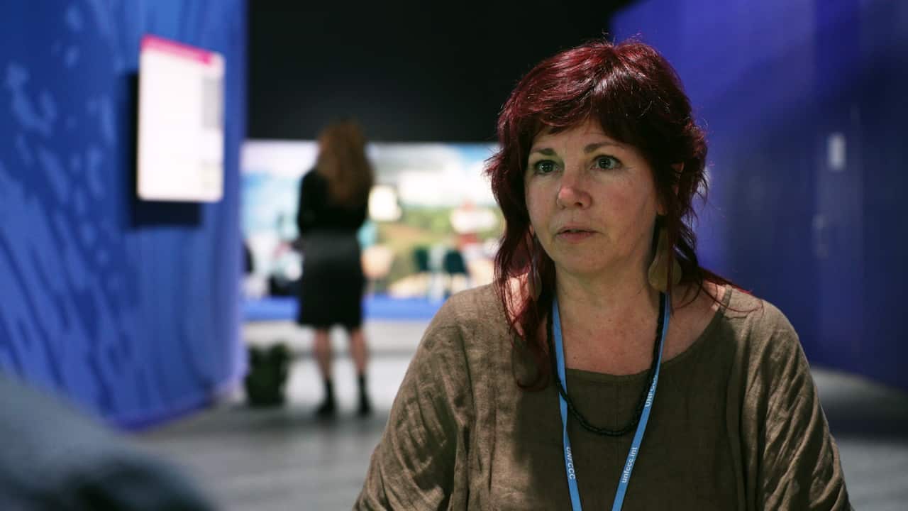 A woman sits in a dark room, with a light behind her. 
