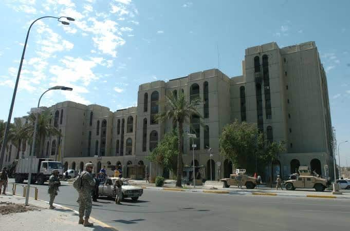 Soldiers in army fatigues and helmets stand on a street with grand Middle Eastern-style buildings.
