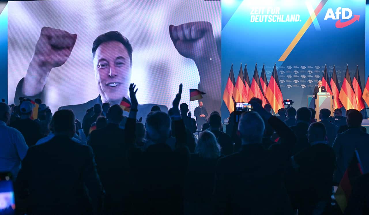 A man with raised fists on a video screen in front of an audience