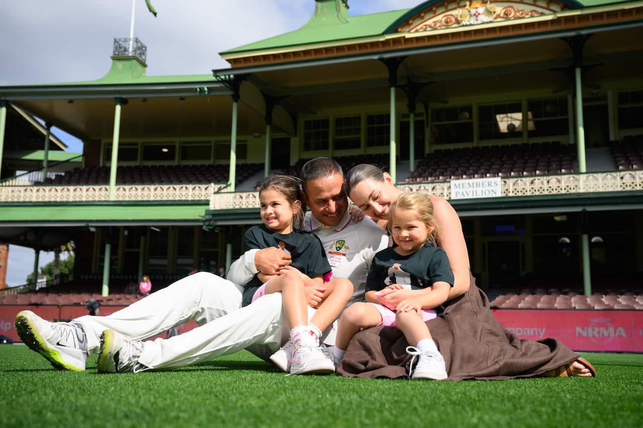 Australian cricketer Usman Khawaja sits on the grass of the Sydney Cricket Ground with his wife and two young daughters.