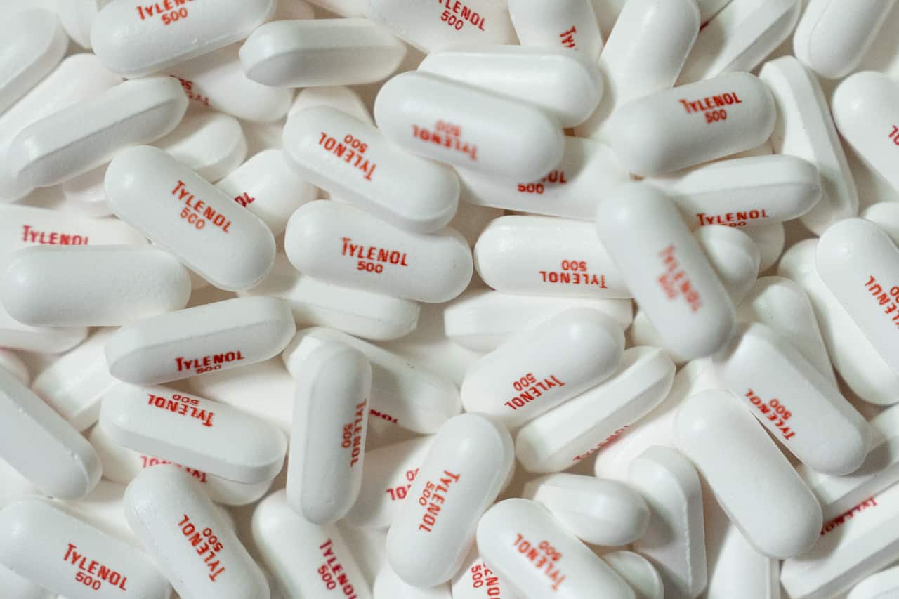 A large pile of white pills that have "Tylenol" marked on them in red.