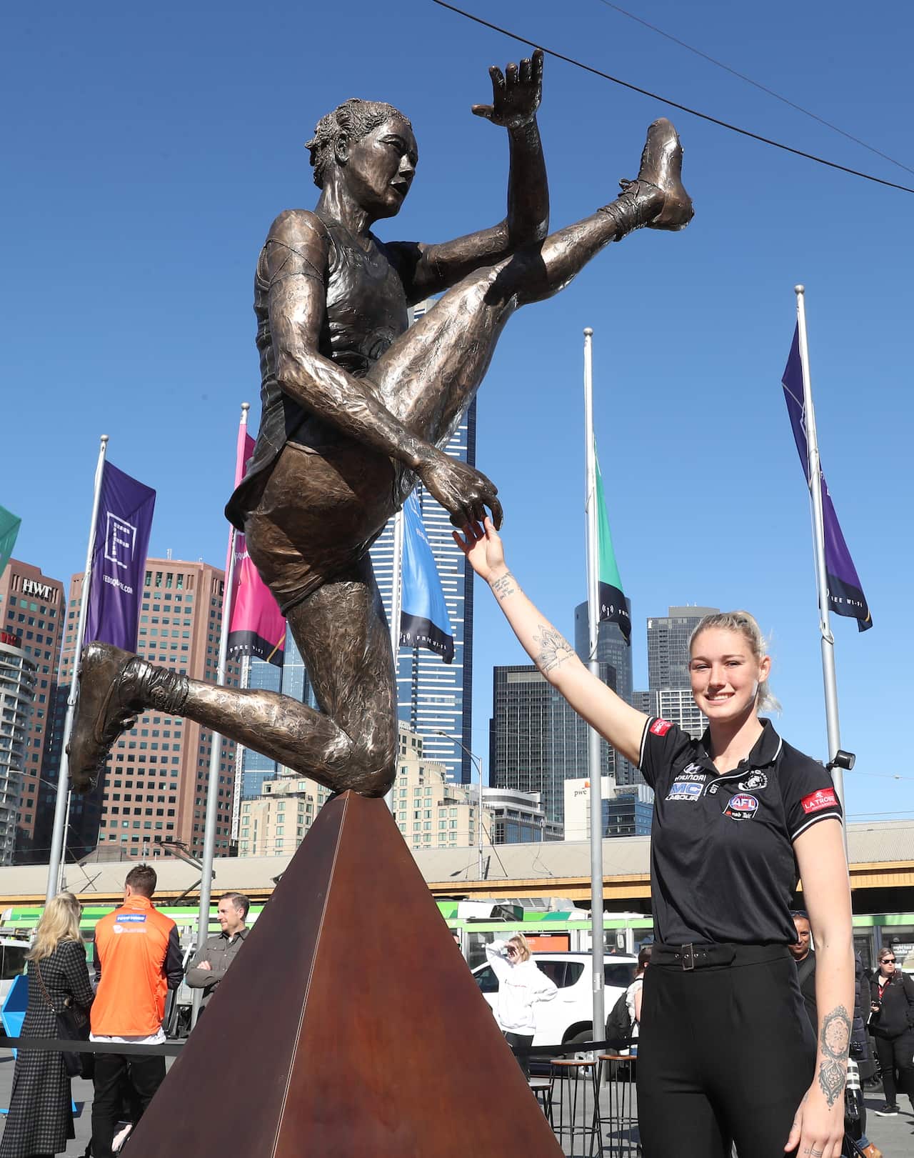 A woman stands next to a bronze statue of herself kicking