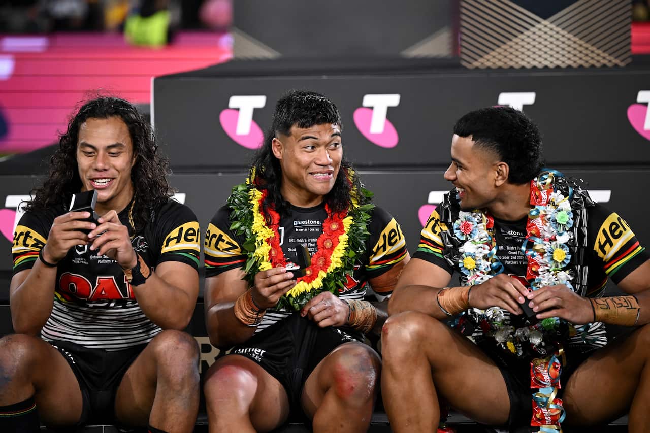 Three Penrith players sit while talking, wearing leis and looking at a ring. 