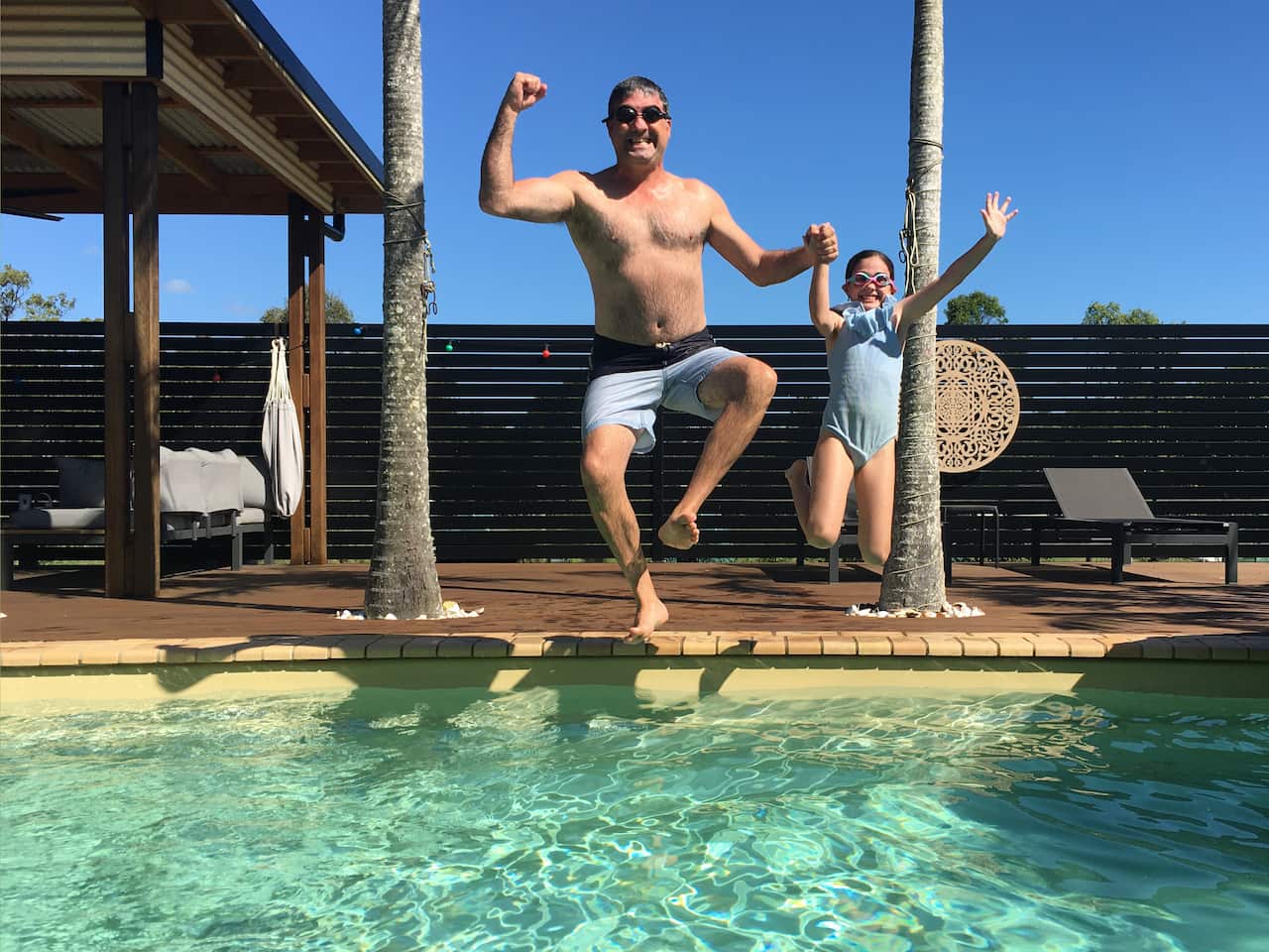 Happy father and daughter jumping together into swimming pool on summer holiday