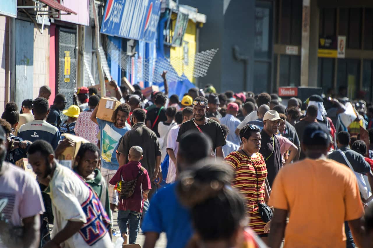 People walking along a street. Some are carrying looted goods.