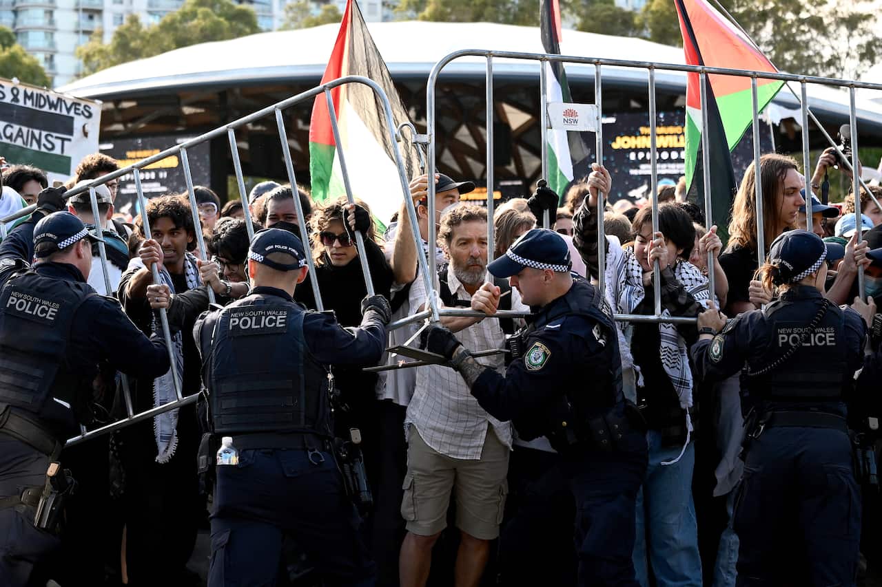 Police hold a metal barrier against a crowd of protesters holding Palestinian flags.