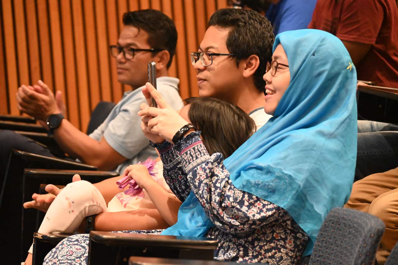 A man, woman and young child sit in chairs in a lecture theatre.