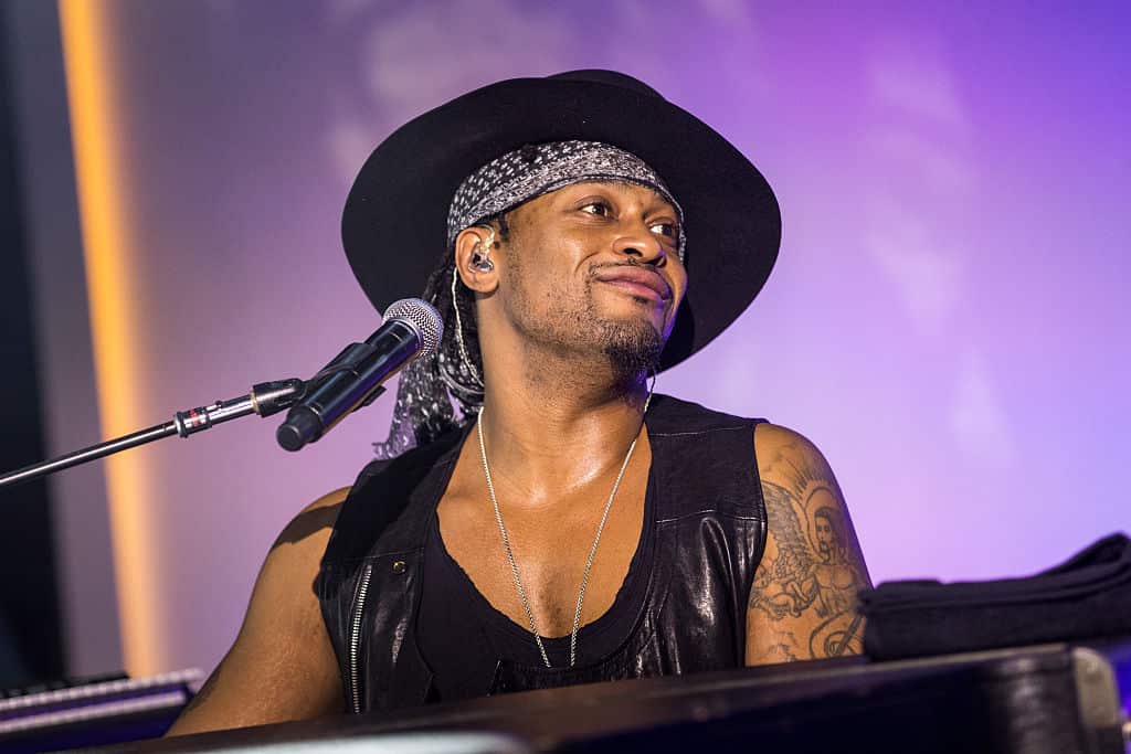 A man performing on stage in a black hat smiles as he looks out to the audience.
