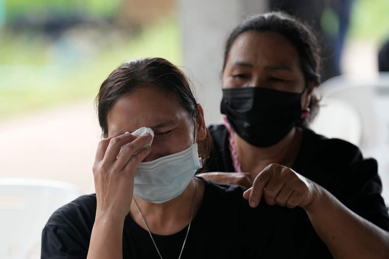 A Thai woman in a face mask cries while another standing behind consoles her