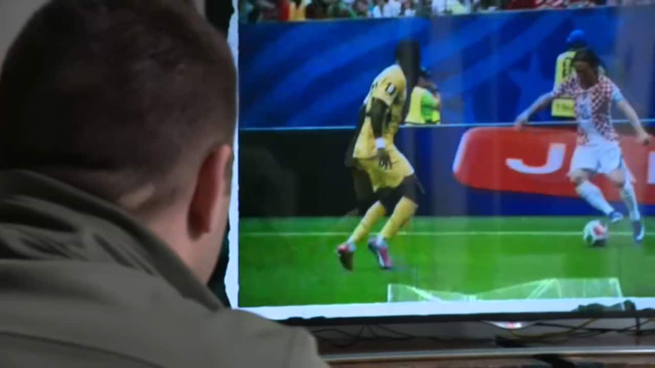 The back of a man's head as he watches sport on TV.