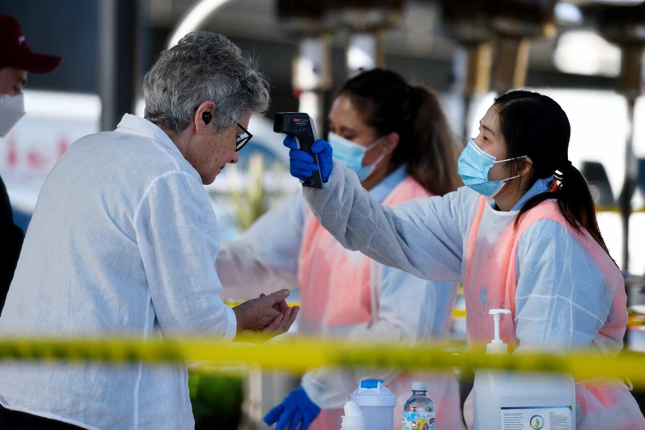 A woman has her temperature taken by another woman holding an instrument to her forehead.