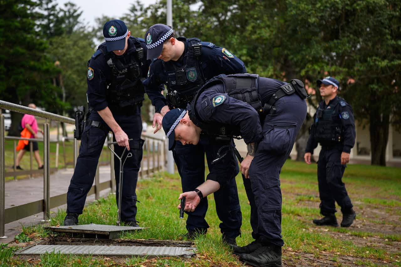 Uniformed police searching a drain in a park 